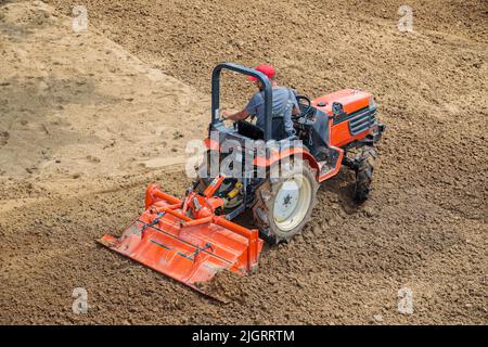 Un agricoltore su un mini trattore allenta il terreno per il prato. Coltivazione di terra, livellamento di superficie. Foto Stock