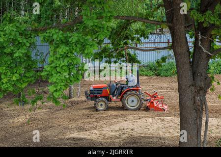 Un agricoltore su un mini trattore allenta il terreno per il prato. Coltivazione di terra, livellamento di superficie. Foto Stock