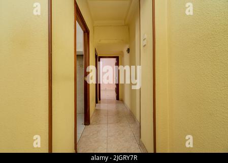 Corridoio dipinto di giallo con ingresso a diverse camere e pavimenti in piastrelle di ceramica Foto Stock