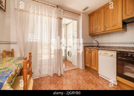 Cucina con mobili rustici in legno, tavolo e sedie coordinati, pavimenti in gres rosso, elettrodomestici da incasso e ripiani in granito rosa Foto Stock