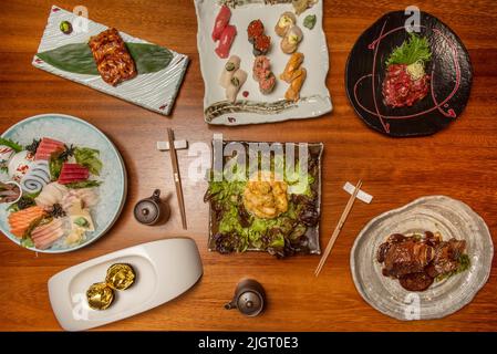 Piatti asiatici preparati con deliziosi sushi sashimi con un sacco di ghiaccio, salmone al forno su foglia di banana e altre ricette su tavola di legno Foto Stock