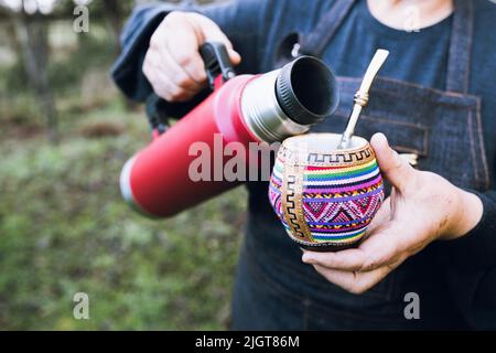 donna irriconoscibile che serve un compagno con un termo rosso, in un colorato compagno etnico. Foto Stock