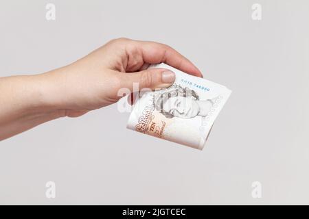 Pila di dieci libbre note della Banca d'Inghilterra in mano femminile. Foto ravvicinata su sfondo grigio della parete Foto Stock