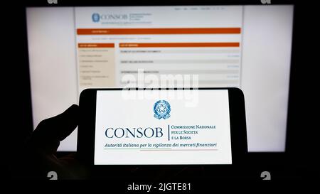 Persona che tiene il cellulare con il logo della Commissione Nazionale per le Societa e la Borsa (CONSOB) su schermo con pagina web. Mettere a fuoco sul display del telefono. Foto Stock