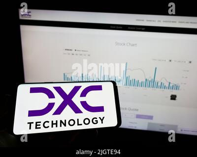 Persona che tiene il telefono cellulare con il logo della società di consulenza IT statunitense DXC Technology Company sullo schermo di fronte alla pagina web. Mettere a fuoco sul display del telefono. Foto Stock