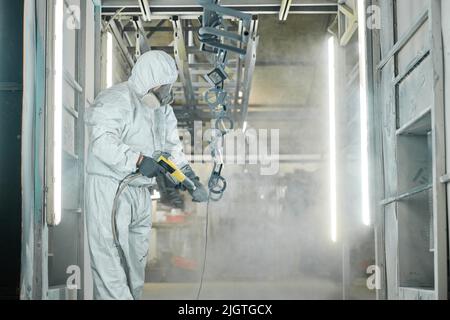 Uomo in tuta protettiva verniciatura a polvere da pistola su prodotti metallici in fabbrica Foto Stock