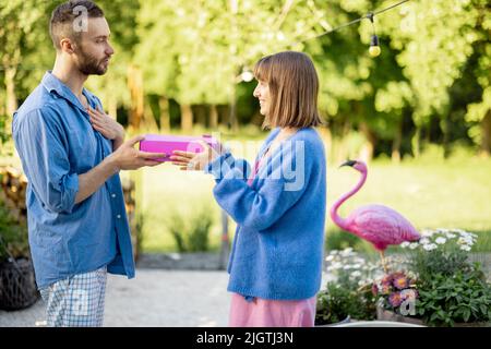 L'uomo dà un regalo in scatola rosa alla sua donna, celebrando all'aperto Foto Stock