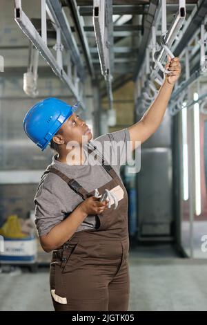 Lavoratrice industriale in hardhat preparare posto per appendere prodotti finiti in magazzino Foto Stock