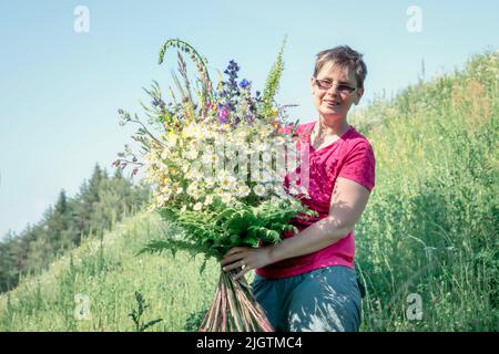 Donna che tiene un grande bouquet di fiori selvatici con margherite di campo nelle sue mani Foto Stock