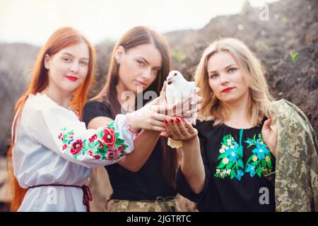 Tre diverse donne ucraine difensori detengono una colomba di pace, un simbolo di pace in Ucraina Foto Stock