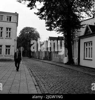 Un paio di edifici residenziali si trovano lungo una strada lastricata. Sulla strada va un uomo. Foto dalla Germania (?). Foto Stock