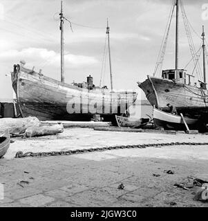 15. Italia. Il giornale fotografico è disponibile presso B.M.A. + Album fotografici. Acquisizione: Libri e materiale di archivio. Foto scattate 1959-10-28,12 Foto in serie. Secondo le note: Italia. Costa Adriatica, Trani, 28/10 -59. Cantieri navali. Un paio di barche sono commissionate a terra in un porto. Un uomo si siede in una delle barche e lavora con l'interno. Foto Stock