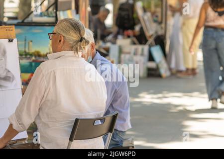 Barcellona, Spagna - 26 maggio 2022: artista di strada in una camicia bianca che dipinge un disegno su una bacheca sulle Ramblas di Barcellona (Spagna). Foto Stock