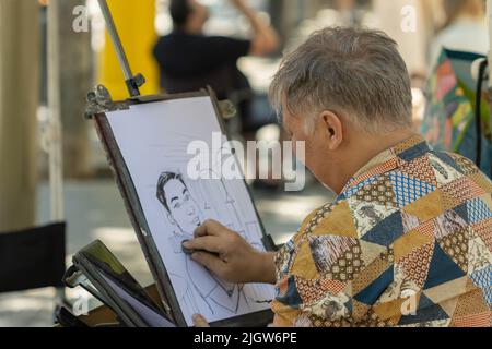 Barcellona, Spagna - 26 maggio 2022: artista di strada che dipinge un disegno su un cartone nelle ramblas di Barcellona (Spagna), fuoco selettivo sul pittore Foto Stock