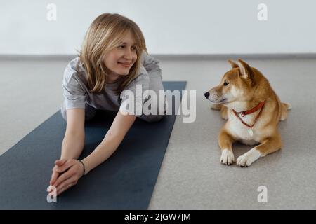 Il cane pratica yoga nella posa della cobra in studio. Le giovani donne meditando con l'animale domestico Foto Stock