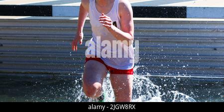 Le ragazze della High School sono molto bagnate dopo essere salite nell'acqua della steeplechase durante una gara su pista Foto Stock