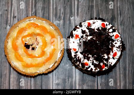 Un dolce della foresta nera, un pan di Spagna al cioccolato, imbevuto di sciroppo di ciliegia con panna montata e ciliegie e un pan di crostata di frutta tropicale con crema Foto Stock