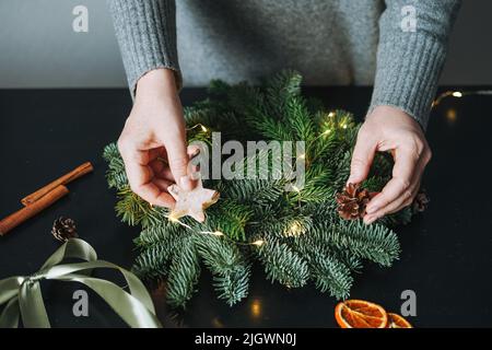 Giovane donna in caldo grigio abito a maglia facendo autocostruire abete natale in mano sul tavolo a casa Foto Stock