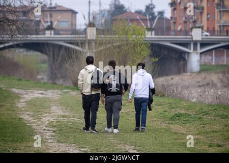 Three Boys Walking sul prato lungo le rive di un fiume asciutto e un ponte sullo sfondo. Foto Stock