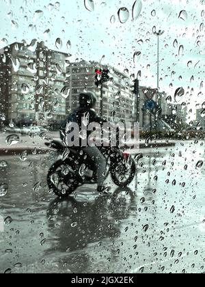 Biker sotto la pioggia dura, immagine sfocata e scura o depressa del biker sotto la pioggia dura. Fuoco selettivo di Raindrops sulla finestra. Biker attesa. Foto Stock