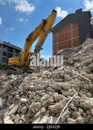 Il frantoio idraulico sta demolendo il vecchio edificio della città. Escavatore giallo parcheggiato sulla parte superiore dei detriti dell'edificio collassati. Foto Stock