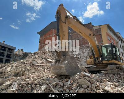 L'escavatore idraulico si trova sulle macerie dell'edificio demolito. Pulizia della vecchia struttura distrutta. Distruzione di edifici disutilizzati. Foto Stock