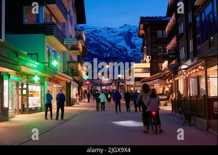 ZERMATT, SVIZZERA - Apr 11, 2022: Turisti che camminano e visitano una strada nella città di Zermatt al tramonto. Foto Stock