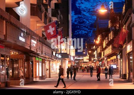 ZERMATT, SVIZZERA - Apr 11, 2022: Turisti che camminano e visitano una strada nella città di Zermatt al tramonto. Foto Stock