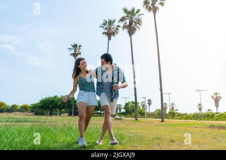 Amici felici che camminano ridendo e tenendosi in un bellissimo parco con palme. Foto Stock