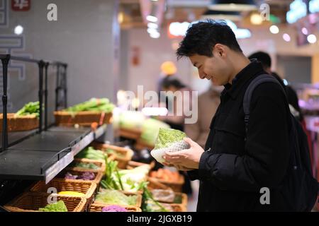 Giovane asiatico che raccoglie verdure nel negozio di alimentari. Uomo sorridente che fa shopping al supermercato Foto Stock