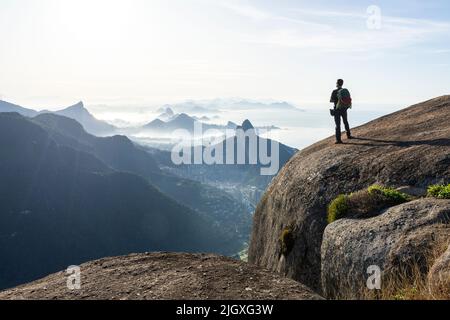 Arrampicatore che gode di una splendida vista sulla città dalla cima rocciosa di montagna Foto Stock