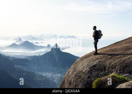 Arrampicatore che gode di una splendida vista sulla città dalla cima rocciosa di montagna Foto Stock