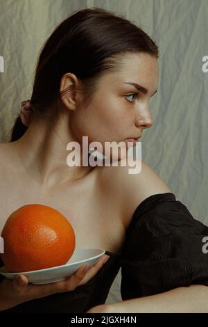 Giovane donna che tiene lateralmente un pompelmo in un piatto Foto Stock