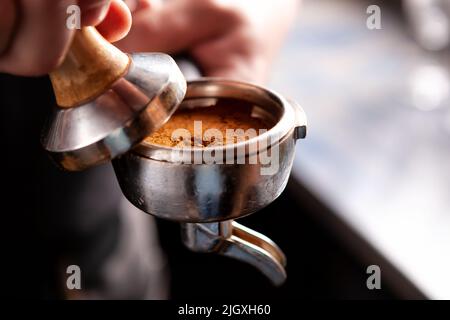 Barista azienda portafilter e caffè rendendo manomissione di un caffè espresso. Foto Stock