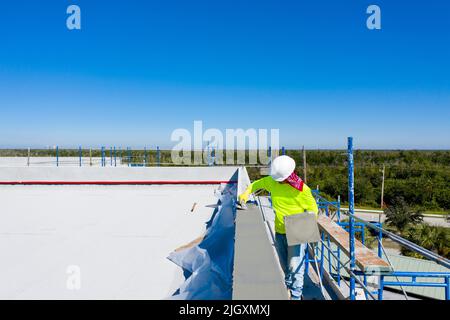 Operaio di costruzione che applica stucco alla plancia / bordo del tetto / parapetto basso di un edificio commerciale vicino a Marco Island, Florida Foto Stock