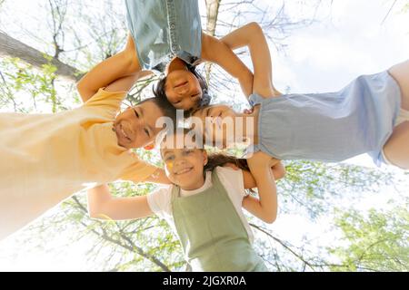 Gruppo di simpatici asiatici e caucasici felici bambini che si accucchiano, guardando giù la macchina fotografica e sorridendo Foto Stock