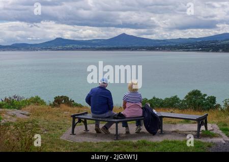 Vista da dietro, una coppia anziana siede su una panchina del Parco di Sorrento, godendo della vista panoramica della baia circondata da montagne. Foto Stock