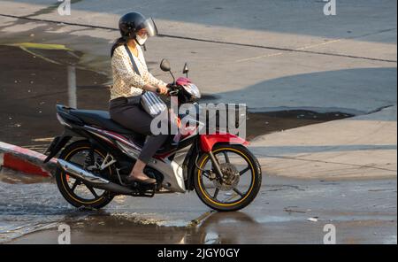 SAMUT PRAKAN, THAILANDIA, 28 2022 FEBBRAIO, Una donna con maschera di faccia corre una moto Foto Stock