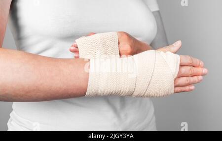 Donna che avvolge la fascia di compressione intorno al polso spruzzato per ridurre il dolore e il gonfiore. Lesioni al braccio. Concetto di assistenza sanitaria. Foto di alta qualità Foto Stock