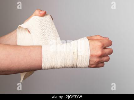 Donna che avvolge un bendaggio elastico intorno al polso doloroso, all'avambraccio. Distorsioni muscolari, trattamento di ceppi. Lesioni al braccio. Concetto di assistenza sanitaria. Foto di alta qualità Foto Stock