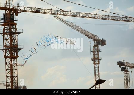 aquilone volante fatto di plastica e legno di vimini con uno sfondo di un cantiere di nuovi edifici, gru e acri di residenza di lusso Foto Stock