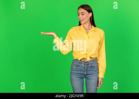 Donna allegra che tiene l'oggetto invisibile a portata di mano su sfondo verde Foto Stock