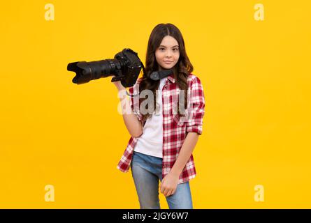 Tutta la lunghezza di ragazza teen con fotocamera professionale dslr con grande obiettivo fotografico. Fotografo di capretto isoalted su sfondo giallo. Scuola di fotografia. Foto Stock