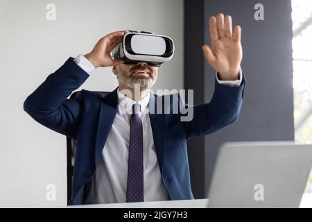 Tecnologie moderne. Un uomo d'affari di mezza età entusiasta che utilizza occhiali VR in ufficio Foto Stock