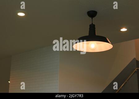 Illuminazione di una lampada a sospensione in ferro con un design semplice appeso in una stanza scarsamente illuminata Foto Stock