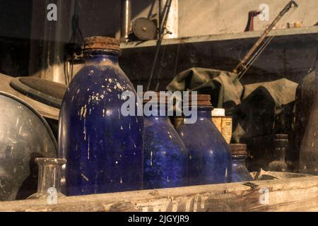 Una collezione di bottiglie d'antiquariato si trova con altri oggetti nella finestra di un negozio abbandonato. Foto Stock