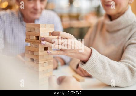 Primo piano di una donna matura si è concentrata sul gioco da tavolo prendendo un piccolo blocco di legno dalla torre giocattolo mentre si gioca con gli amici Foto Stock