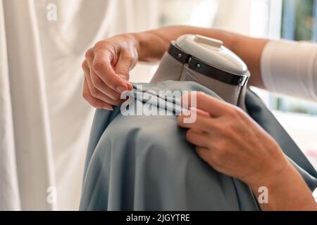le mani seamstress creano pieghe in un indumento su un manichino Foto Stock