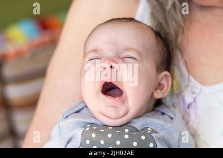 Ritratto heartwarmming di una ragazza del bambino carina di un mese tenuta vicino al petto della nonna. Imbardata del bambino esaurita con gli occhi chiusi. Con spazio di copia. Foto Stock