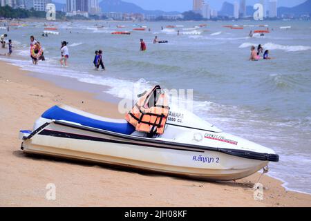 Una moto d'acqua sulla spiaggia aspetta i clienti mentre le persone giocano in mare oltre a Jomtien, Pattaya, Thailandia, Asia. Foto Stock